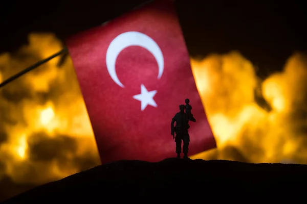 Turkey small flag on burning dark background. Concept of crisis of war and political conflicts between nations. Silhouette of armed soldier against a Turkish flag. Selective focus