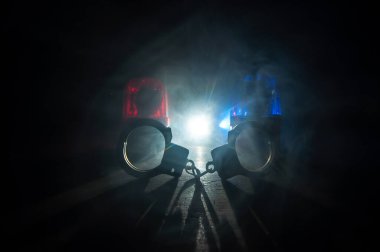 Gece polis baskını ve sen tutuklusun. Arka tarafında polis arabası olan kelepçelerin silueti. Görüntü sisli arka planda yanıp sönen kırmızı ve mavi polis ışıkları. Seçici odak