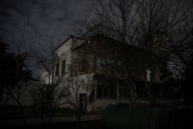 Geceleri ormanda bir hayaletin olduğu eski bir ev ya da terk edilmiş bir korku evi. Ölü ağaç ormanındaki eski mistik bina. Gerçeküstü ışıklar. Korku Cadılar Bayramı konsepti
