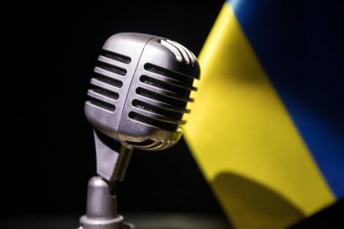 Bulanık bir Ukrayna bayrağının arka planındaki mikrofon. Karanlık masa dekorasyonu. Seçici odak