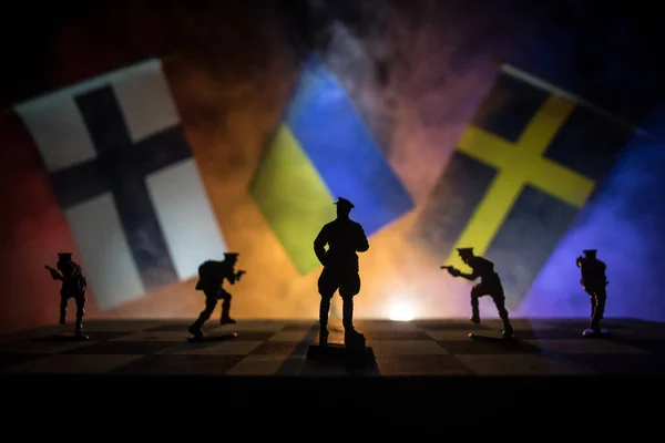 Flags of Sweden, Finland and Ukraine on dark background. Conceptual image of war between Russia and countries using toy soldiers and national flags . Selective focus