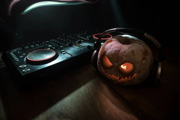 Halloween pumpkin on a dj table with headphones on dark background with copy space. Happy Halloween festival decorations and music concept