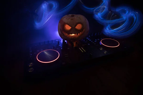 Halloween pumpkin on a dj table with headphones on dark background with copy space. Happy Halloween festival decorations and music concept