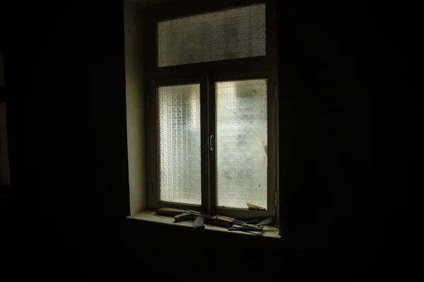 Conceptual photo of war between Russia and Ukraine. Russian weapon (rifle) on windowsill at night. Old creepy room with window. Explosion outside.