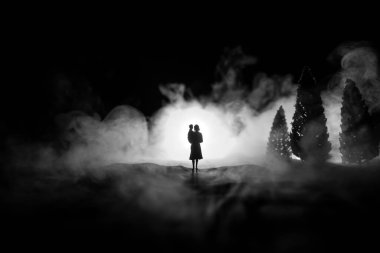 Geceleri mezarlıkta çocuklu bir kadının silueti dolaşıyor. Korku Cadılar Bayramı konsepti. Işık ve dumanla sanat masası dekorasyonu. Seçici odak