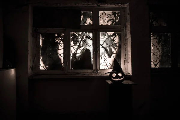 Scary Halloween pumpkin in the mystical house window at night or halloween pumpkin and horror silhouette in window. Selective focus