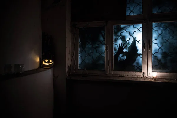 Scary Halloween pumpkin in the mystical house window at night or halloween pumpkin and horror silhouette in window. Selective focus