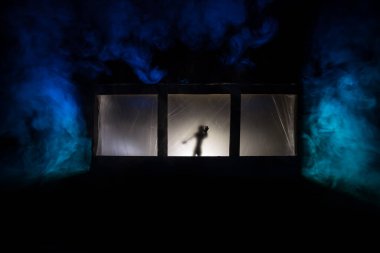 Sanat dekorasyonu. İçinde büyük pencereler ve zombiler olan eski bir ev. Penceredeki bulanık korkunç siluetler. Korku Cadılar Bayramı konsepti