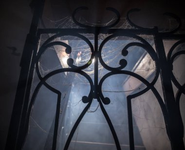 Korku Cadılar Bayramı konsepti. Ürkütücü terk edilmiş kale. Eski bir şamdan ve cadılar bayramı balkabağı tahta merdivenlerde parlıyor ve geceleri kafes kapılı. Arkaplan ışığı ve sisli dekorasyon. Seçici odak