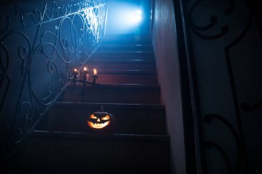 Korku Cadılar Bayramı konsepti. Ürkütücü terk edilmiş kale. Eski bir şamdan ve cadılar bayramı balkabağı tahta merdivenlerde parlıyor ve geceleri kafes kapılı. Arkaplan ışığı ve sisli dekorasyon. Seçici odak