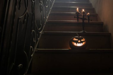 Korku Cadılar Bayramı konsepti. Ürkütücü terk edilmiş kale. Eski bir şamdan ve cadılar bayramı balkabağı tahta merdivenlerde parlıyor ve geceleri kafes kapılı. Arkaplan ışığı ve sisli dekorasyon. Seçici odak