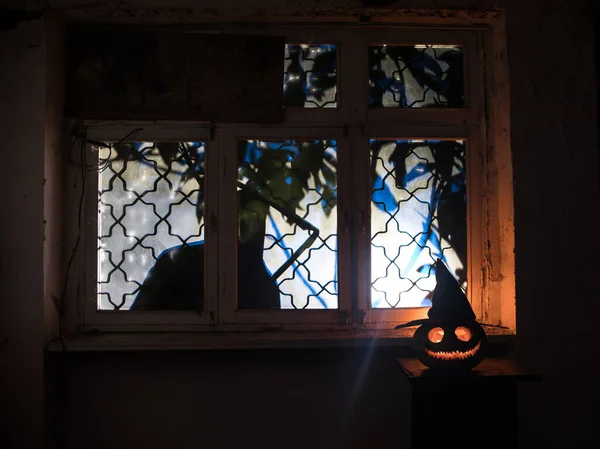 Scary Halloween pumpkin in the mystical house window at night or halloween pumpkin and horror silhouette in window. Selective focus