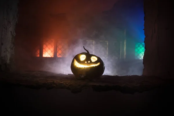 Scary Halloween pumpkin in the mystical house window at night or halloween pumpkin in night on abandoned room with window. Selective focus