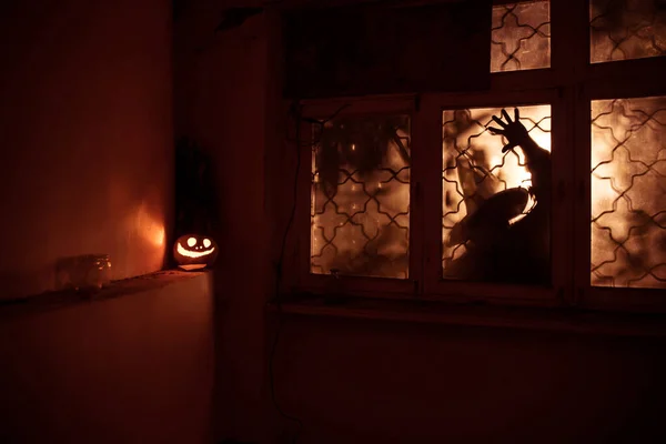 Scary Halloween pumpkin in the mystical house window at night or halloween pumpkin and horror silhouette in window. Selective focus