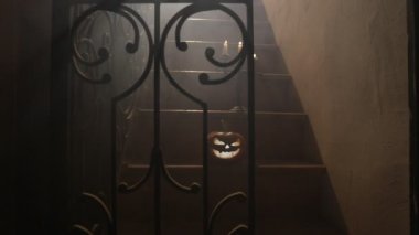 Korku Cadılar Bayramı konsepti. Ürkütücü terk edilmiş kale. Eski bir şamdan ve cadılar bayramı balkabağı tahta merdivenlerde parlıyor ve geceleri kafes kapılı. Arkaplan ışığı ve sisli dekorasyon. Seçici odak