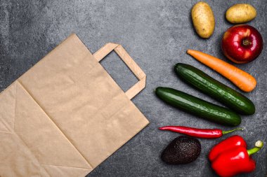 Sağlıklı yemek geçmişi. Çantada sağlıklı vejetaryen yemeği var. Sebzeler ve meyveler siyah taşın üzerinde. Süpermarkette yiyecek alışverişi. Temiz vejetaryen yeme konsepti.
