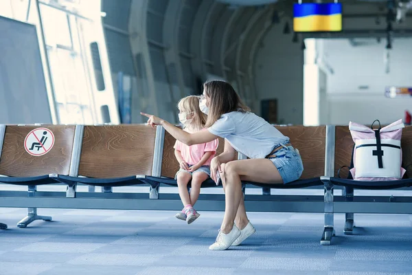 Matka z córką w maskach czeka na ich lot na lotnisku. Kobieta z małą dziewczynką w międzynarodowym lotnisku. — Zdjęcie stockowe