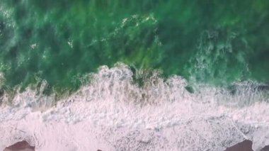 Güçlü fırtınalı deniz dalgaları İHA atışından yukarıdan görünüyor. Kumsal ve deniz köpüklü beyaz dalgalarla.