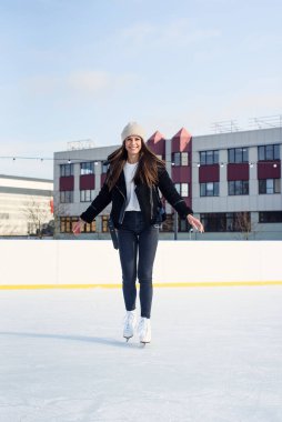 Şık ceketli güzel bir kadın eğleniyor, buz pateni pistinde gülüyor. Neşeli genç bayan Noel buz pateni pistinde kayıyor. Kış tatili dışarıda