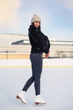 Şık ceketli güzel bir kadın eğleniyor, buz pateni pistinde gülüyor. Neşeli genç bayan Noel buz pateni pistinde kayıyor. Kış tatili dışarıda