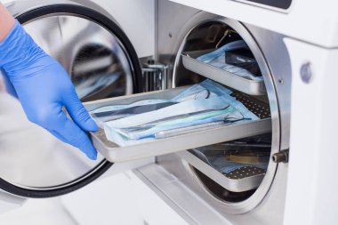 Asistanlar eldivenlerini teslim edip sterilize etmek için otoklava paketlenmiş diş aleti takıyorlar..