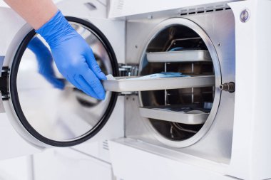 Asistanlar eldivenlerini teslim edip sterilize etmek için otoklava paketlenmiş diş aleti takıyorlar..