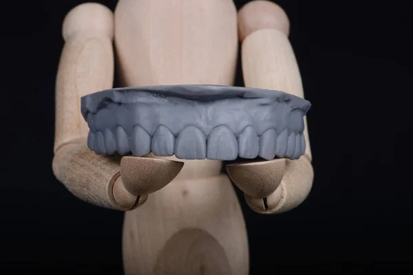 Lidská dřevěná figurka drží v rukou model zubní horní čelisti vytištěný na 3D tiskárně na černém pozadí. — Stock fotografie