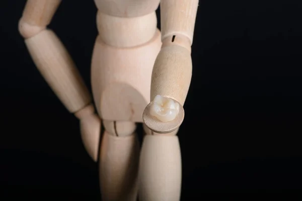 A figura de madeira humana mantém em mãos uma ponte de zircônia com o glazour em um fundo preto. — Fotografia de Stock
