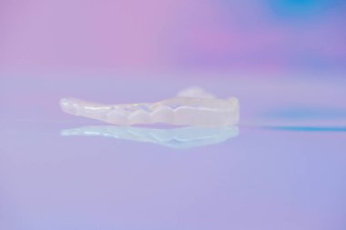 Açık renkli arkaplanda polimerden yapılmış 3 boyutlu şeffaf diş kapağı. Bruksisizme karşı diş bandı.