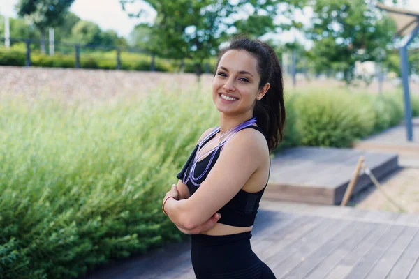 Portrait of smiling young woman with jump rope at outdoor exercising. Fitness female doing skipping workout outdoors on a sunny day.