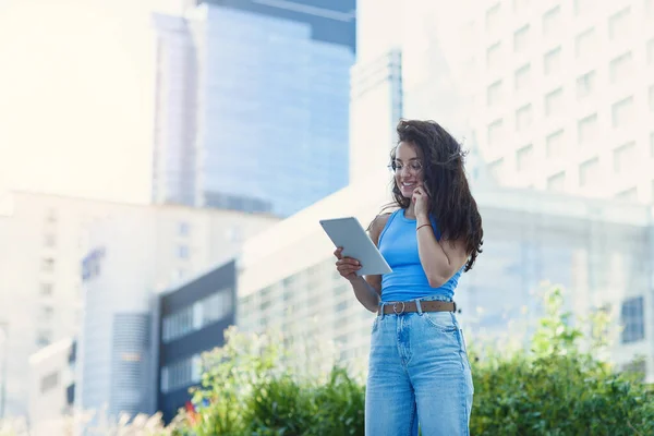 Attractive female office worker with tablet has a working conversation near modern office building. Happy office worker concept.