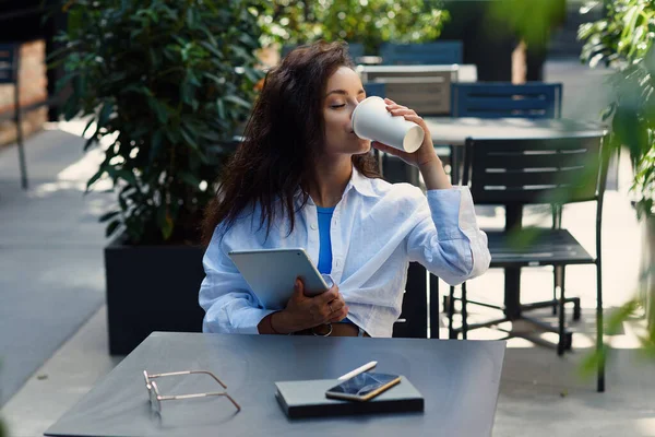 Young business woman drinking coffee and working with tablet in cozy street cafe.