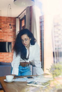 Gözlüklü genç ve güzel bir iş kadını serbest ofis masasında iş belgeleriyle çalışıyor..