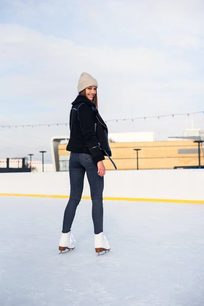 Happy beautiful woman at stylish jacket having fun, laugh on outdoor ice skating rink. Cheerful pretty young woman skate on Christmas ice rink. Winter holiday outside activity