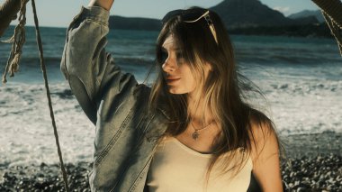 Kız salıncakta oturuyor, tek eliyle tutuyor ve yana bakıyor.