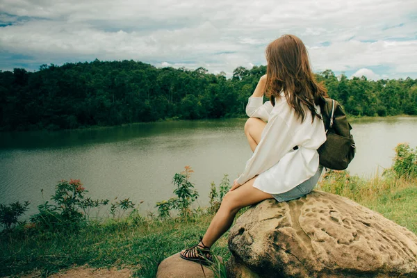 Genç Asyalı yalnız kadın yazın dağların arasında nehrin kenarında taşın başında otururken. Beyaz bir gömlek ve omuz çantası giyiyordu, sorunlarını düşünüyordu ve çok üzgündü..