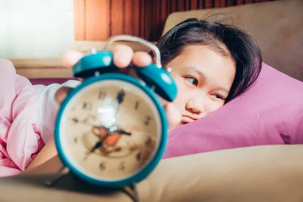Unhappy girl waking up in bed with alarm clock. Young girl in the morning. Students wake up early to go to school.