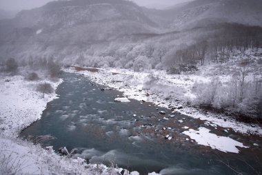 the Kuban mountain river at the mouth of the mountain slopes of Karachay-Cherkessia in winter with a snow-covered valley