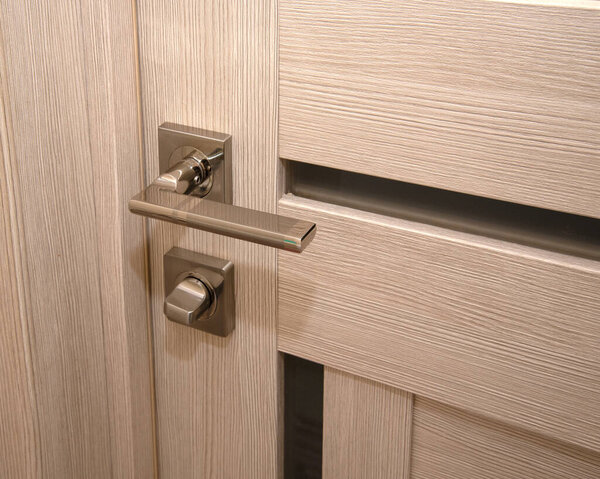 A modern, shiny door handle on a light-colored new interior door