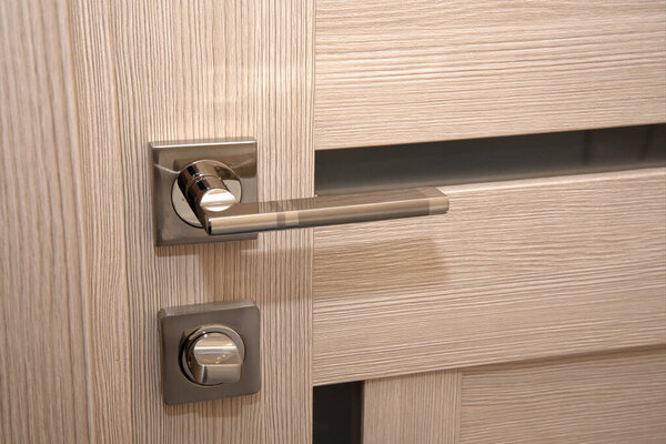 A modern, shiny door handle on a light-colored new interior door