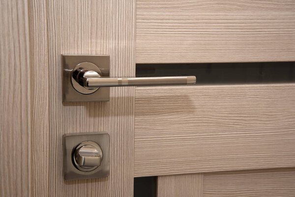 A modern, shiny door handle on a light-colored new interior door
