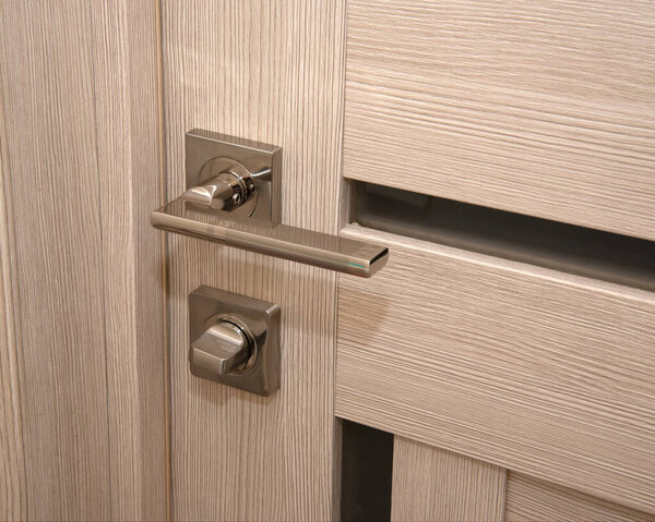 A modern, shiny door handle on a light-colored new interior door