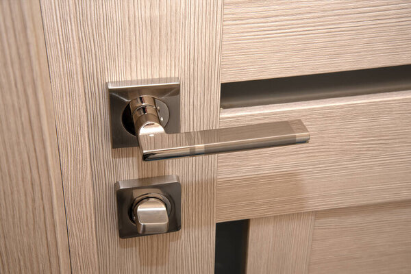 A modern, shiny door handle on a light-colored new interior door