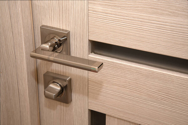 A modern, shiny door handle on a light-colored new interior door