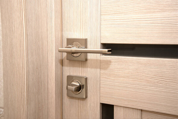 A modern, shiny door handle on a light-colored new interior door