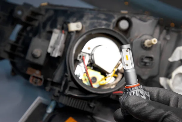gloved hand holding a car lamp for replacement in a car headlight