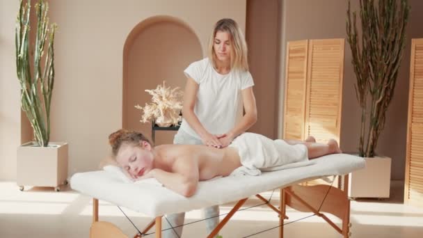 Vista completa de la mujer feliz recibiendo masaje en el spa. Joven hembra acostada en el salón de masajes mientras la mujer la masajea — Vídeos de Stock