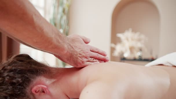 Cropped view of the man lying on the towel with closed eyes. Massage therapist standing on the background next to him and massaging — Stock Video