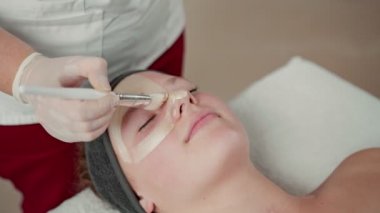 Genç kızın kırpılmış görüntüsü güzellik salonunda yüz prosedürünün keyfini çıkarıyor. Yalan söylüyor ve zevkle kilden maske takıyor.