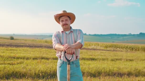 Portré fotó a kaukázusi jóképű férfi mezőgazdasági dolgozó kalapban áll a területen, nézi a kamera és a kezében lapát — Stock videók
